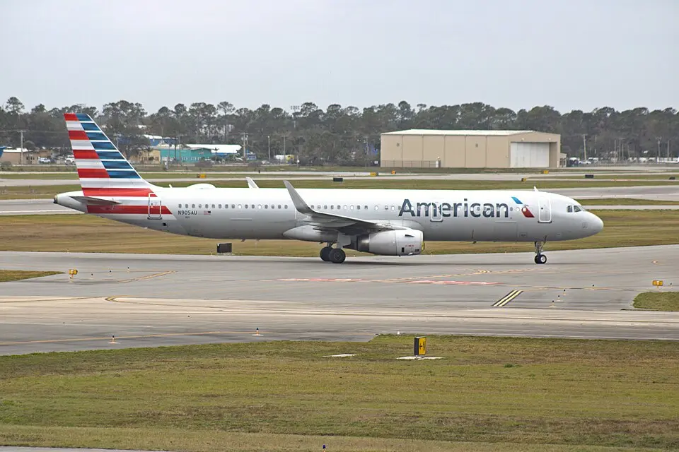 American Airlines Airbus A321 taxiing past a hangar and tree line